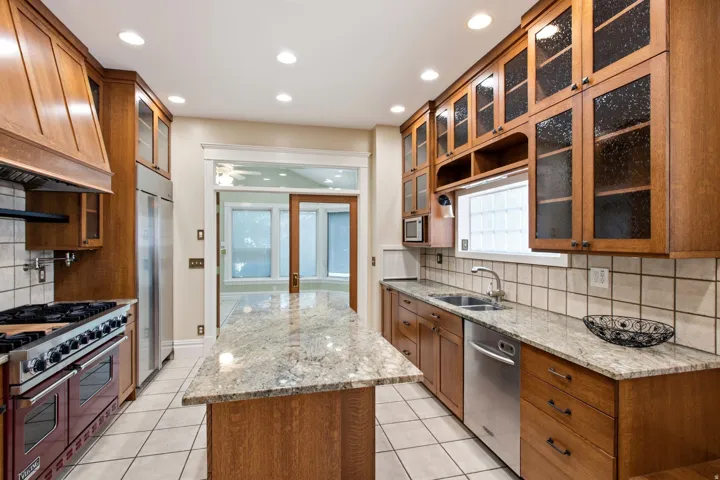 Kitchen featuring a central island with a light-toned countertop, extensive wood cabinetry, stainless steel appliances, a tiled backsplash, and recessed lighting