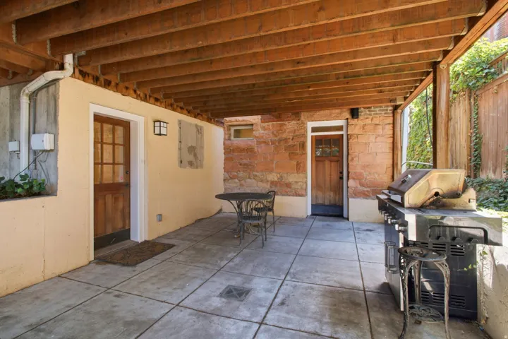 Covered patio area featuring a concrete slab, exposed wood beam ceiling, and two wood-paneled doors with glass inserts