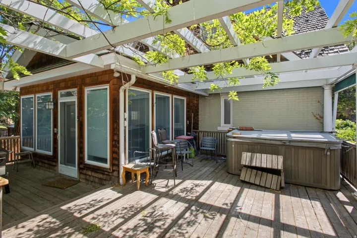 Spacious outdoor deck featuring a hot tub, a pergola with overhead greenery, and a sunroom addition with multiple windows and a screen door