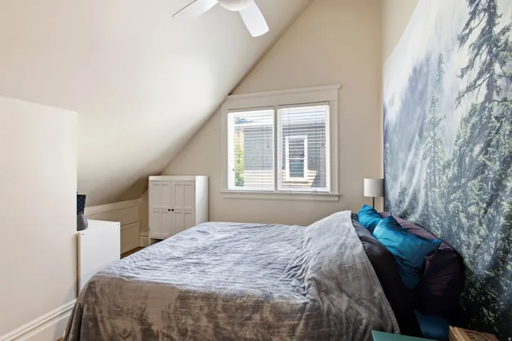 Attic bedroom featuring an angled ceiling, white ceiling fan, and a double window with blinds