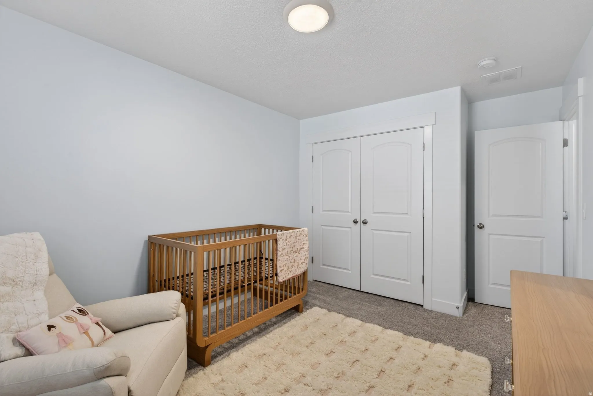 Bright room featuring light blue walls, neutral-toned carpeting, a flush-mount ceiling light fixture, and white bi-fold closet doors with panel detailing
