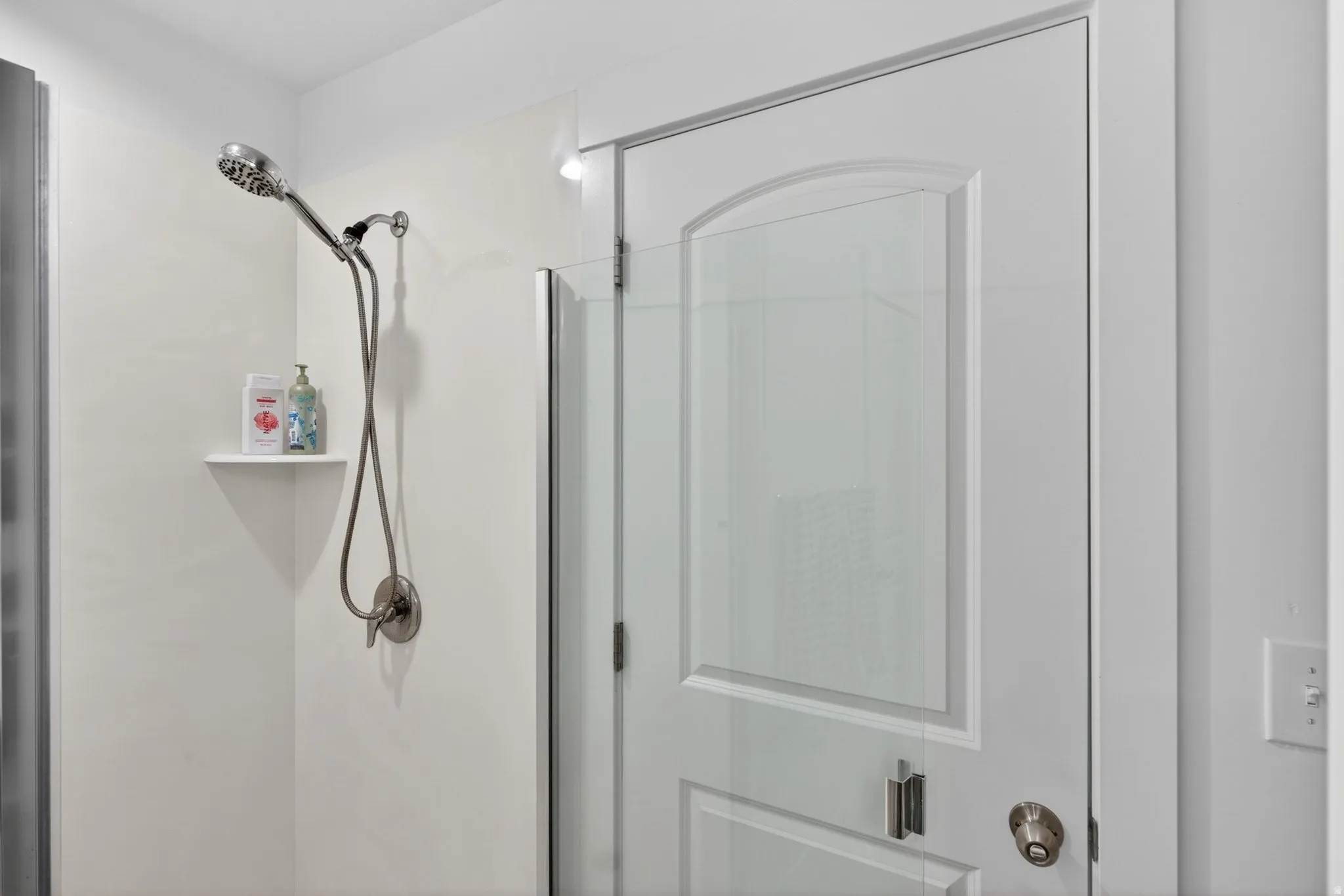 Brushed nickel shower fixture with a handheld wand and a built-in corner shelf