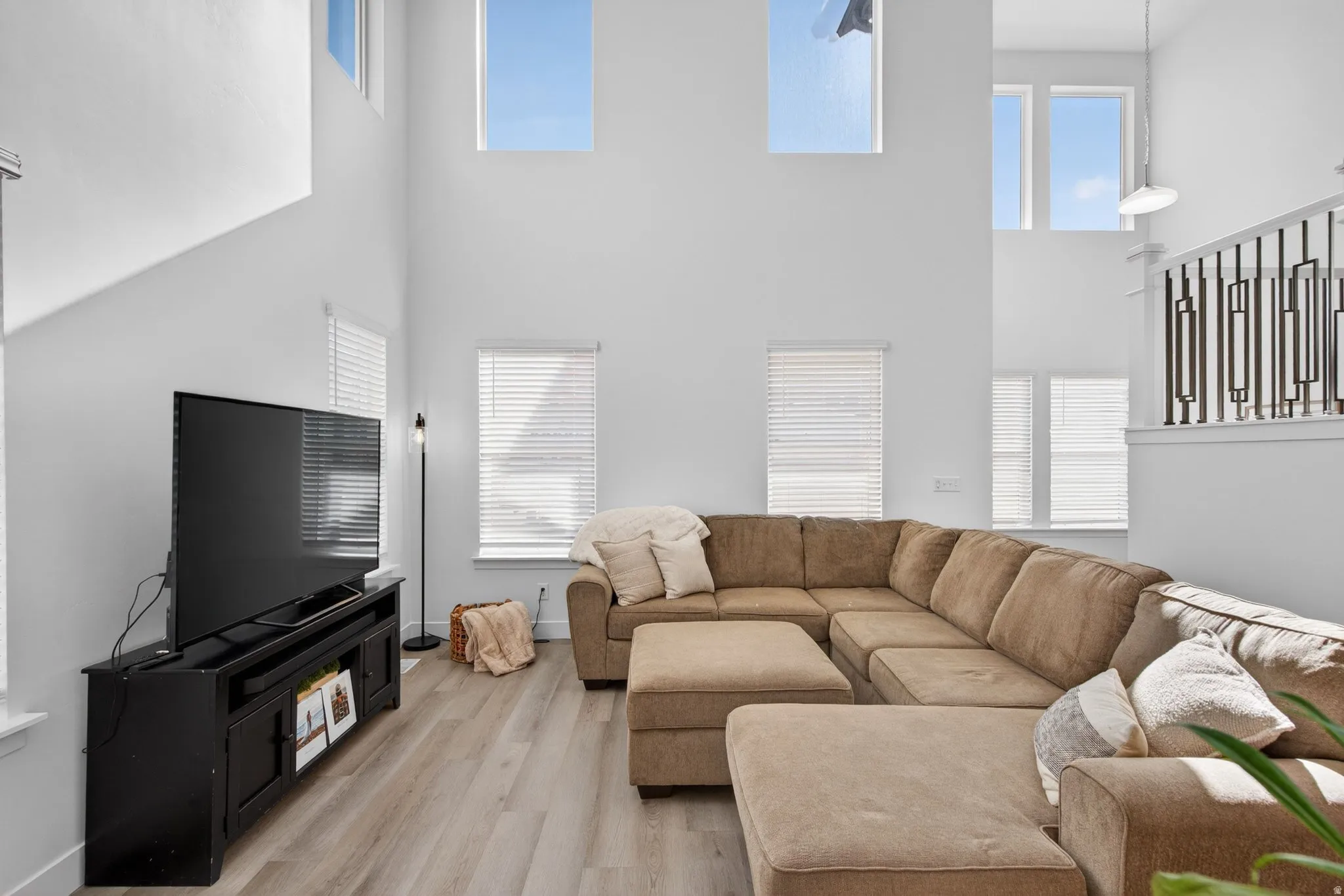 Two-story living area featuring high ceilings with upper windows, wood-finish flooring, and multiple lower windows with blinds