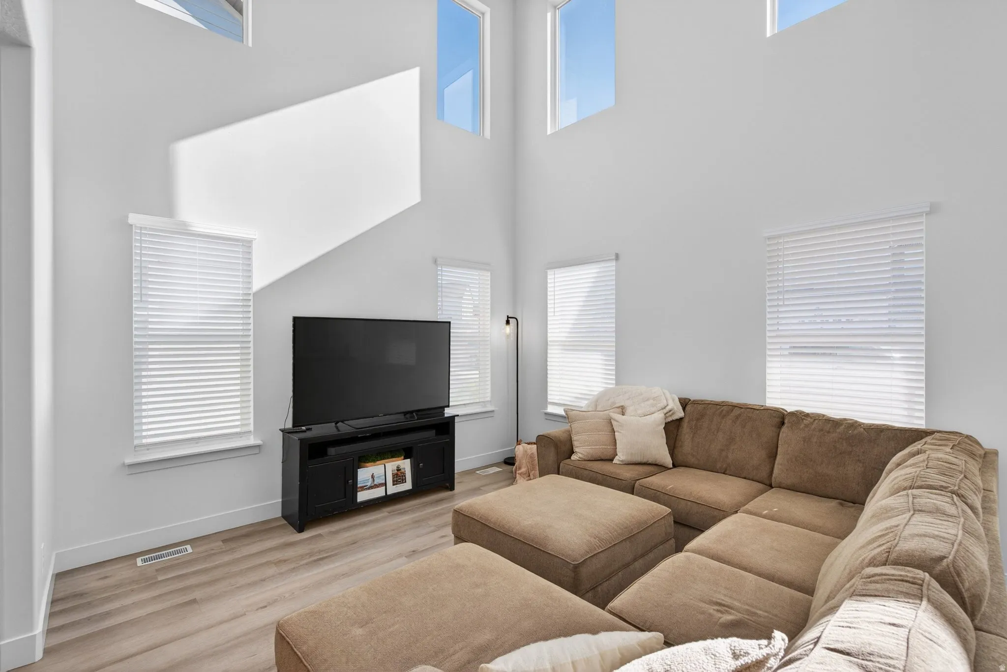Living area featuring high ceilings, upper transom windows, recessed windows, wood-finish flooring, and crisp white walls
