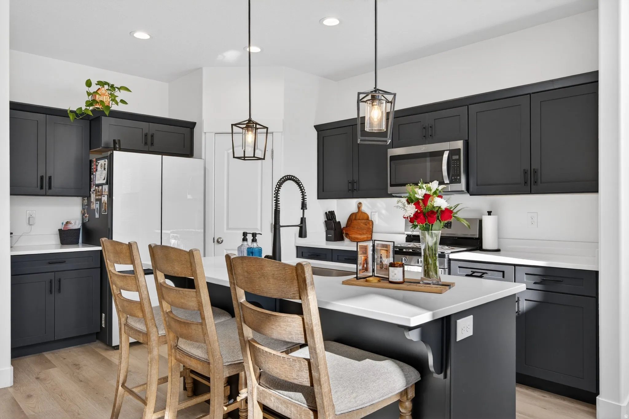 Modern kitchen featuring dark cabinetry, white countertops, a central island with seating, a stainless steel microwave, and wood-finish flooring