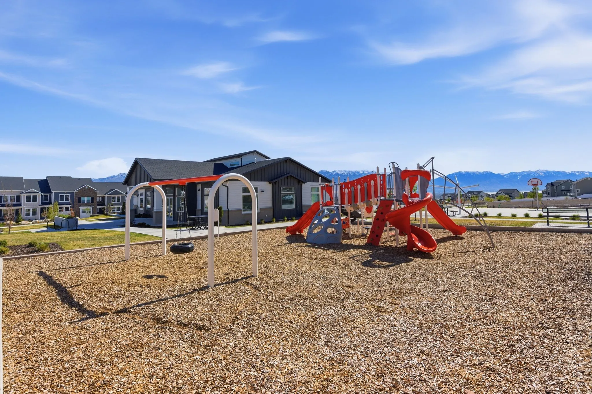 Community playground featuring a swing set, multi-level play structure with slides, and wood chip surfacing