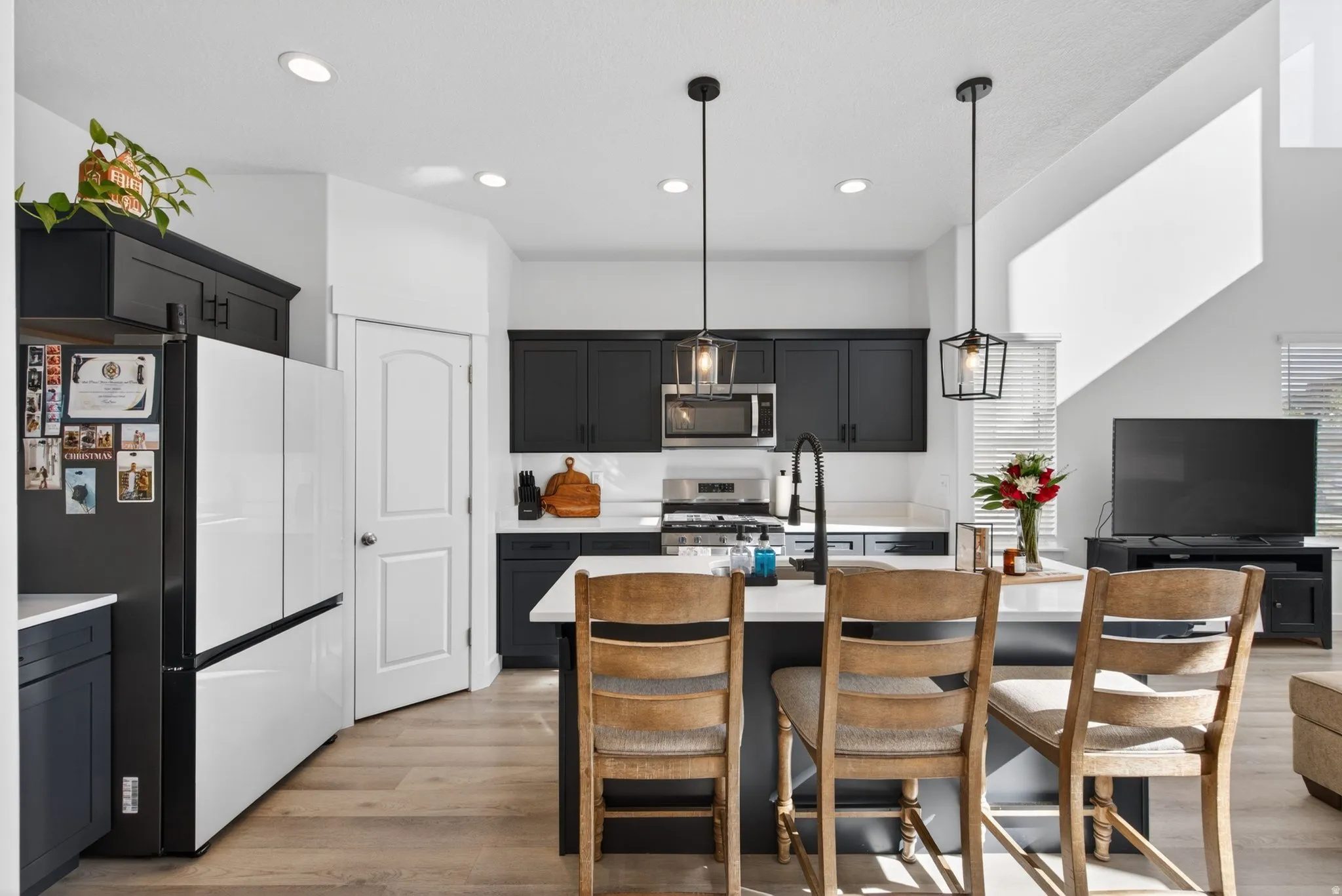 Modern kitchen featuring dark cabinetry, stainless steel appliances, a center island with seating, pendant lighting, and wood-finish flooring