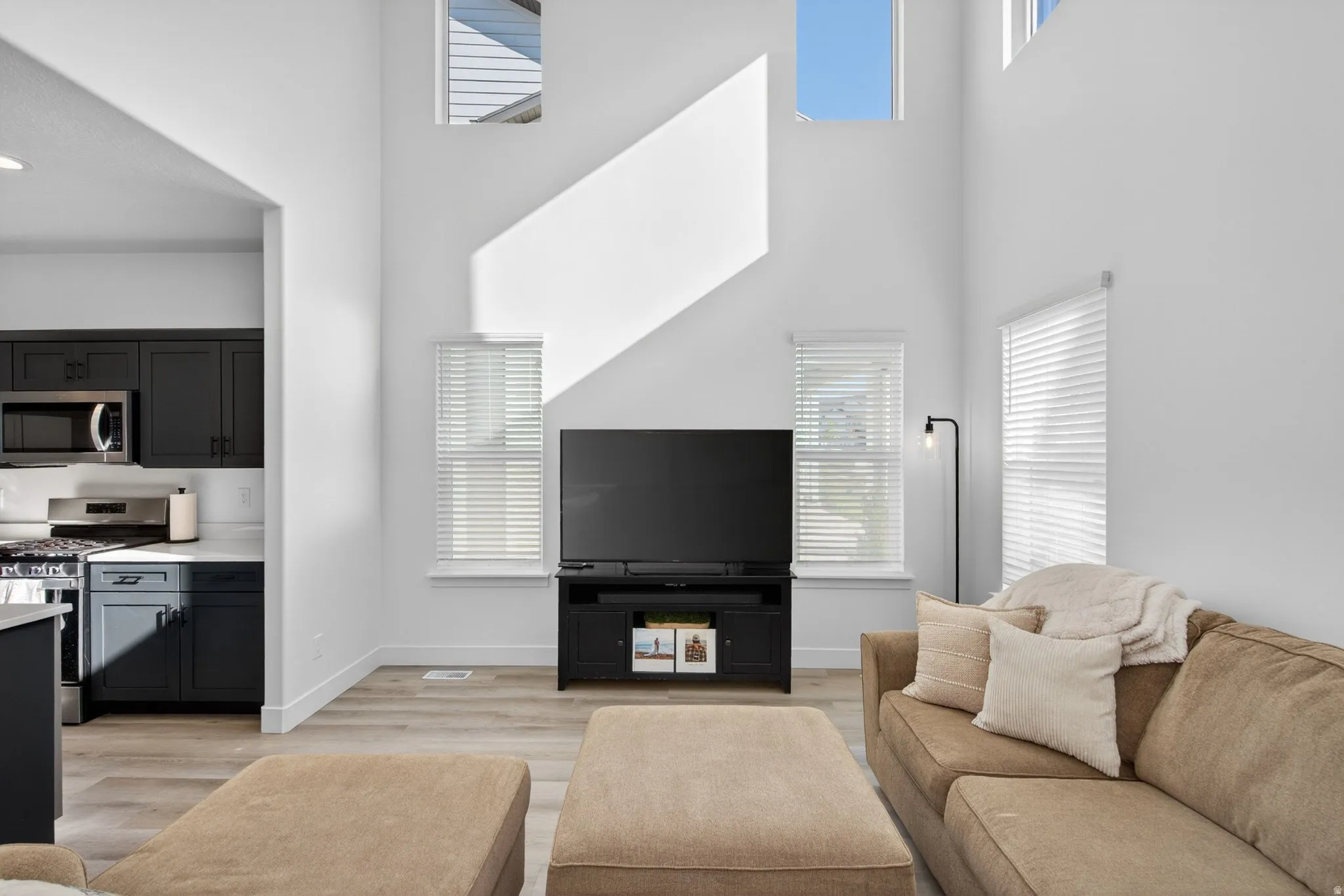 Two-story living area with high ceilings, multiple windows, and wood-finish flooring