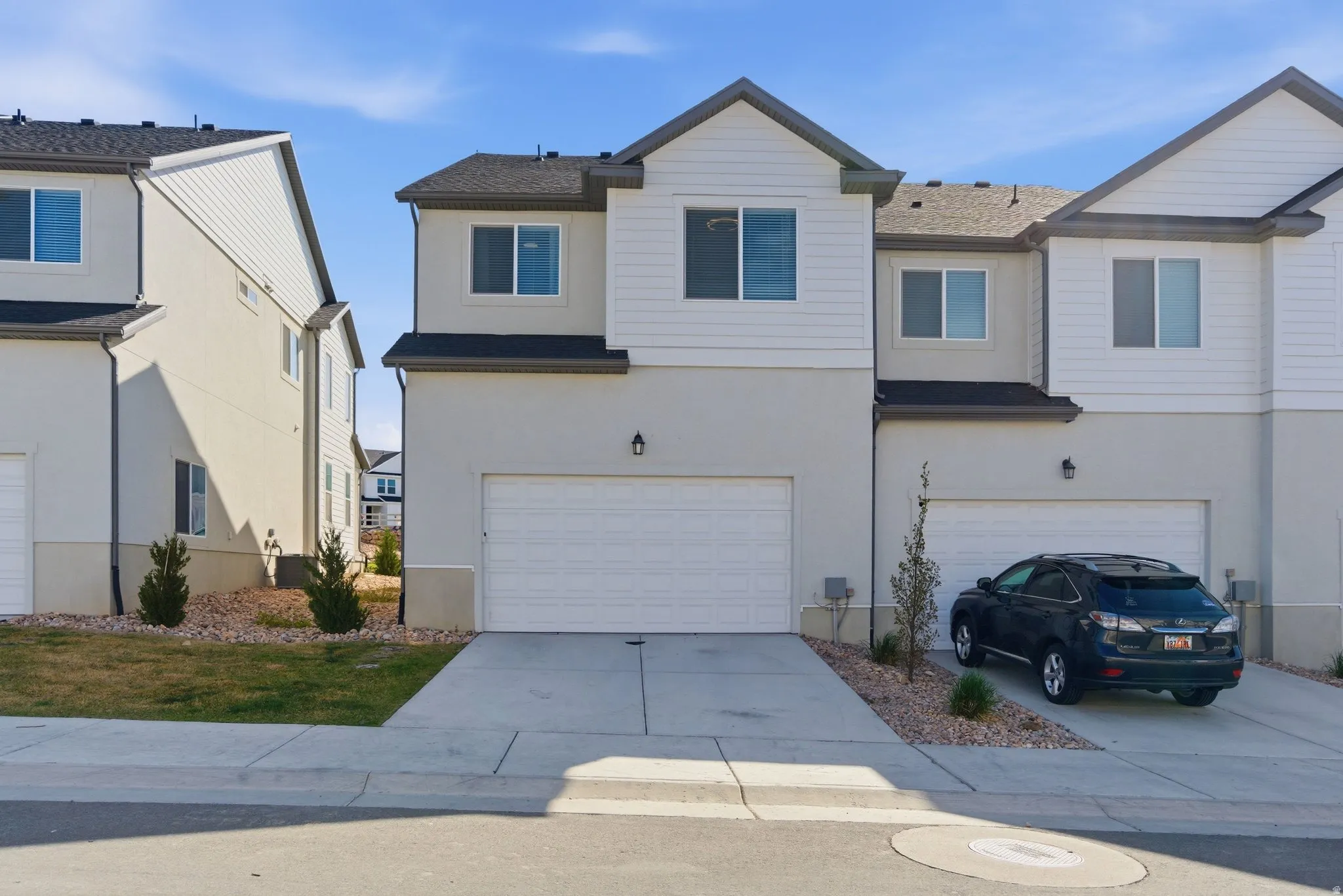 Contemporary townhome featuring a two-car garage, light stucco and siding exterior, dark shingle roofing, and concrete driveway