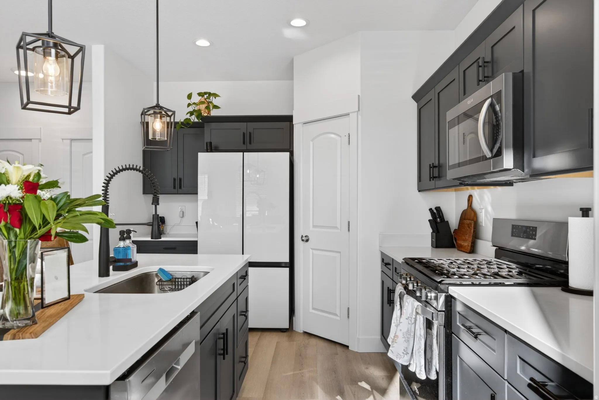 Modern kitchen featuring dark cabinetry, white countertops, stainless steel appliances, a kitchen island with a sink, and wood-finish flooring