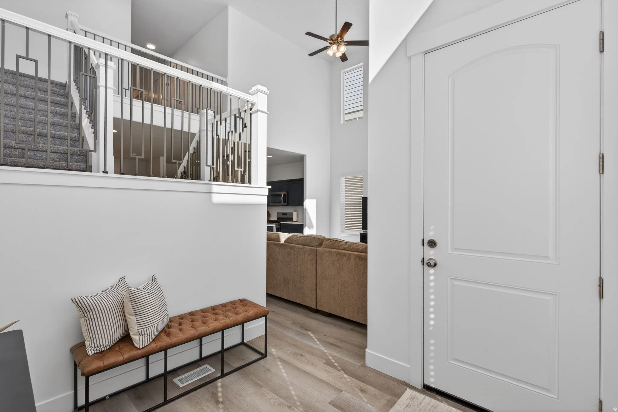 Entryway featuring high ceilings, wood-finish flooring, a contemporary staircase with decorative metal balusters, and a solid panel front door
