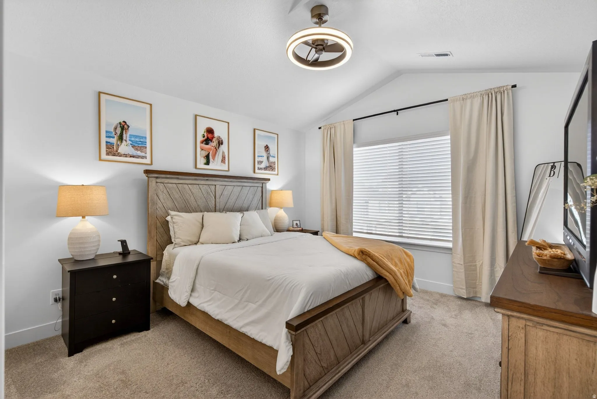 Spacious bedroom featuring vaulted ceilings, a large window with blinds, soft carpet flooring, and a modern ceiling fan