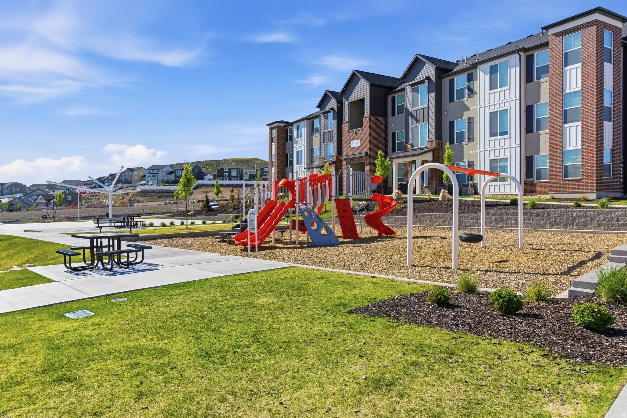 Outdoor common area featuring a modern playground with multiple slides and a tire swing, alongside a picnic area with concrete pathways