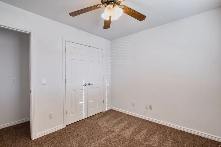 Room featuring a ceiling fan with light fixture, white bi-fold closet doors, and brown carpet flooring