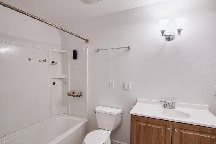 White tub and shower combination with built-in shelving, wood-finish vanity with integrated sink, and wall-mounted light fixture