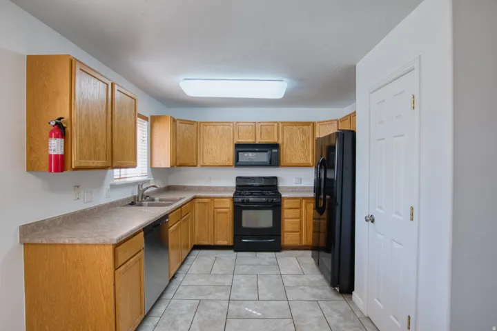 Kitchen featuring wood-finish cabinetry, a stainless steel dishwasher, black appliances, and tiled flooring