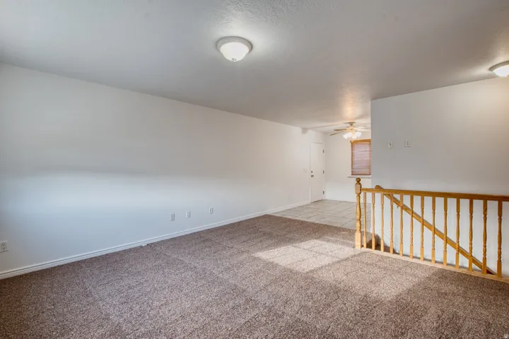 Carpeted living area featuring white walls, flush-mount lighting, and a wood railing