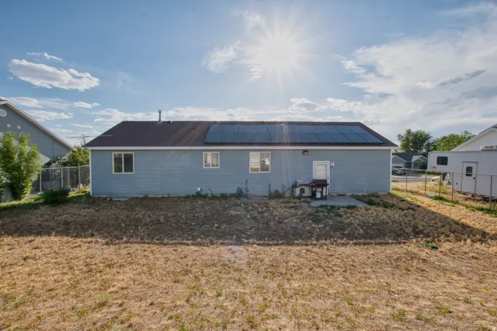 Rear exterior featuring light blue siding, multiple windows, a dark shingle roof, and roof-mounted solar panels