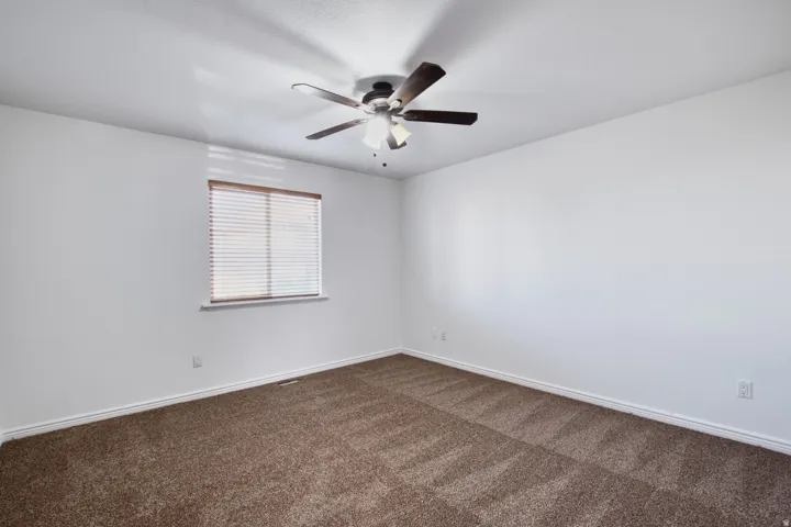 Room featuring brown patterned carpeting, white walls, a single window with blinds, and a ceiling fan with light fixture