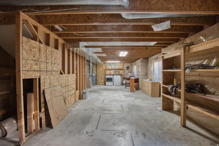 Unfinished basement space featuring exposed wooden joists, concrete flooring, framed partition walls, and built-in wooden shelving units