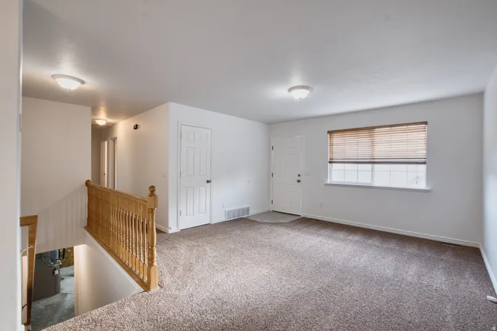 Carpeted living area featuring a multi-pane window with blinds, a white paneled entrance door, and a wooden banister