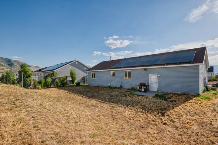 Rear exterior with light blue siding and a brown shingled roof featuring multiple solar panels