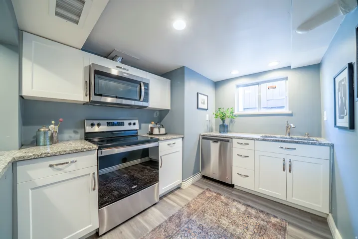 Compact kitchen featuring white shaker-style cabinetry, stainless steel appliances, speckled stone countertops, and wood-finish flooring