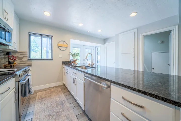 Kitchen featuring dark speckled countertops, white shaker cabinetry, stainless steel appliances, and wood-finish tile flooring