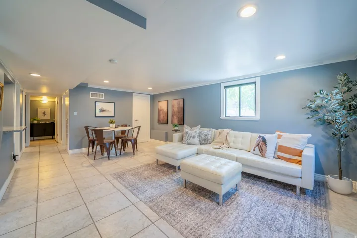 Spacious open-concept room featuring light-toned tile flooring, recessed lighting, crown molding, and a window providing natural illumination