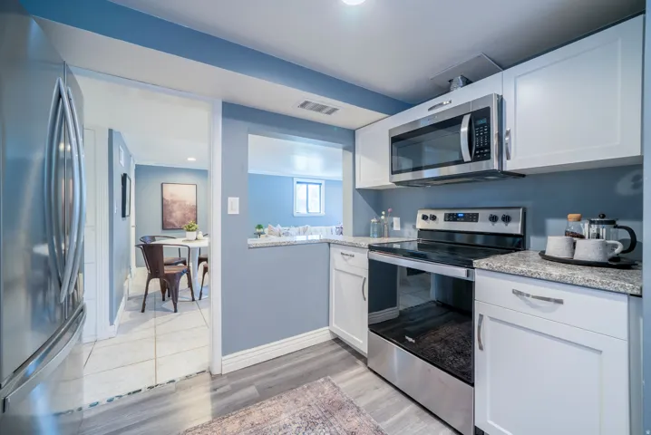 Kitchen featuring white cabinetry, stainless steel appliances, granite-style countertops, and wood-finish flooring