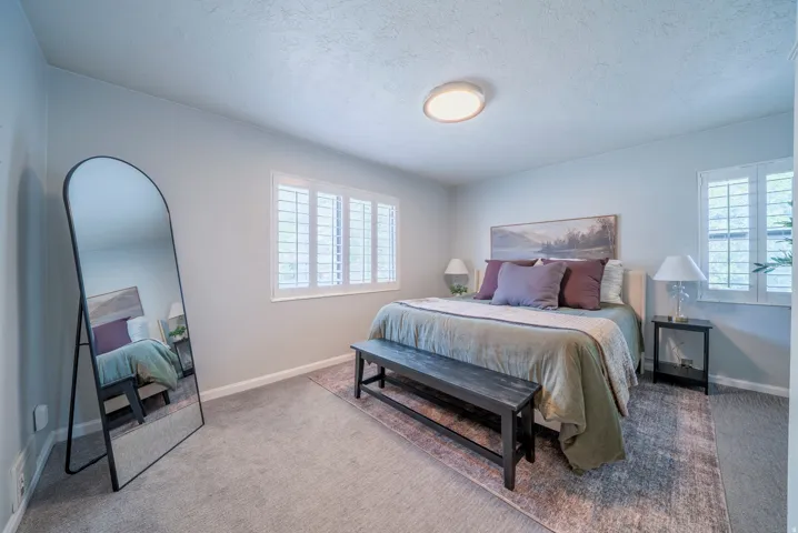 Bedroom featuring wall-to-wall carpeting, dual windows with plantation shutters, a ceiling-mounted light fixture, and light-toned wall finishes