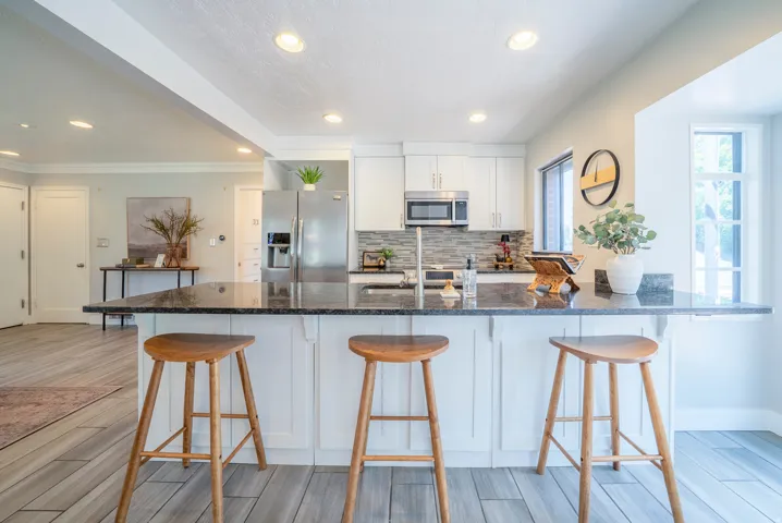 Kitchen featuring a breakfast bar with stone countertop, white cabinetry, stainless steel appliances, and wood-finish flooring