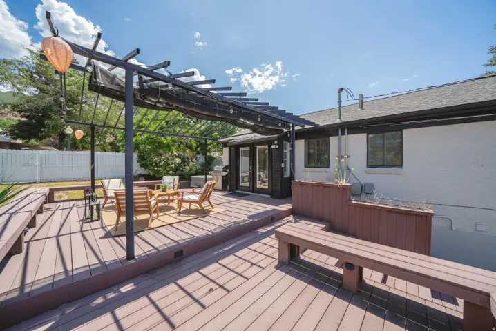 Multi-level deck featuring a pergola with a retractable shade cover, built-in benches, and double glass doors leading into the property