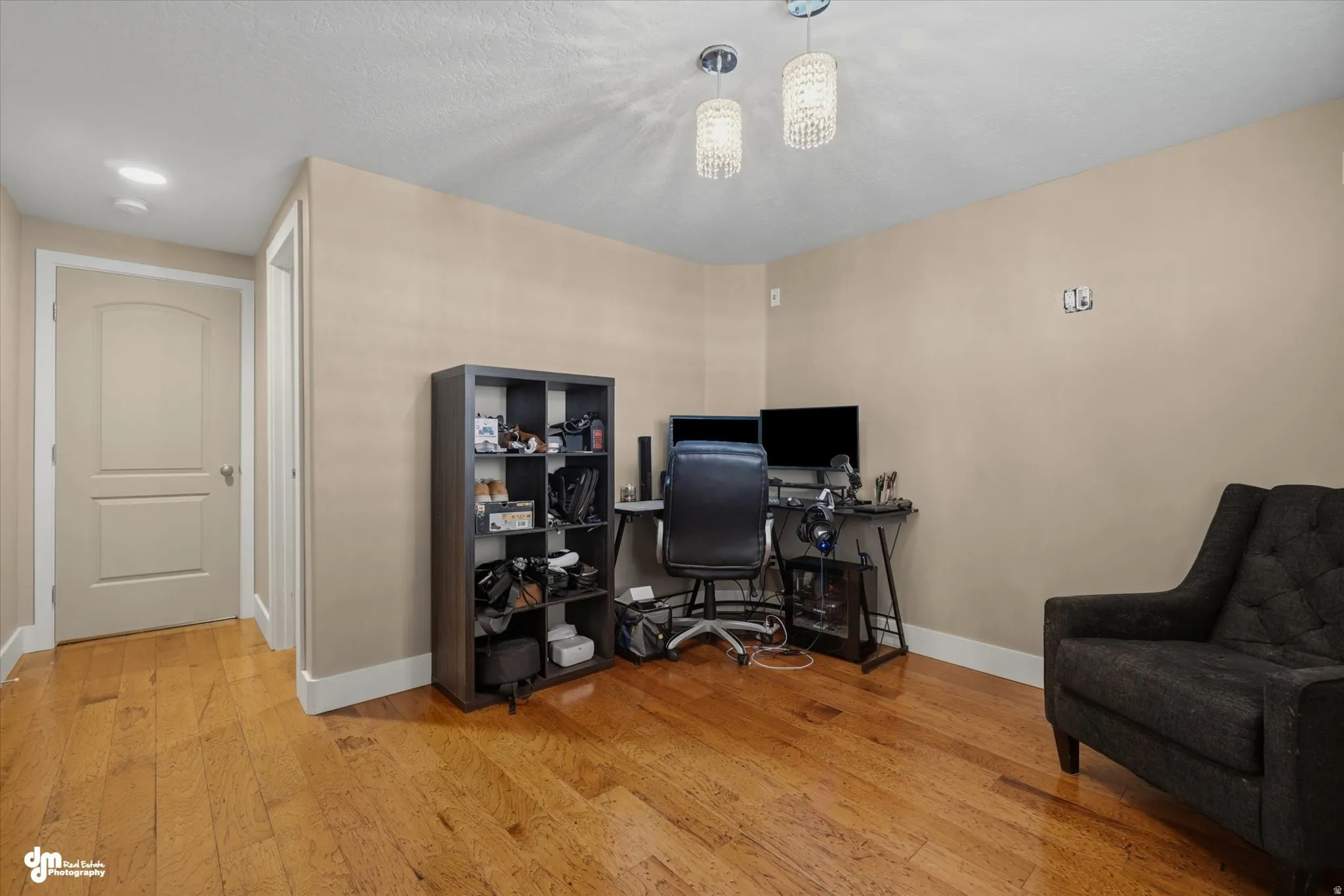 Spacious room featuring wood-finish flooring, neutral-toned walls, white baseboards, and a white ceiling with two pendant light fixtures