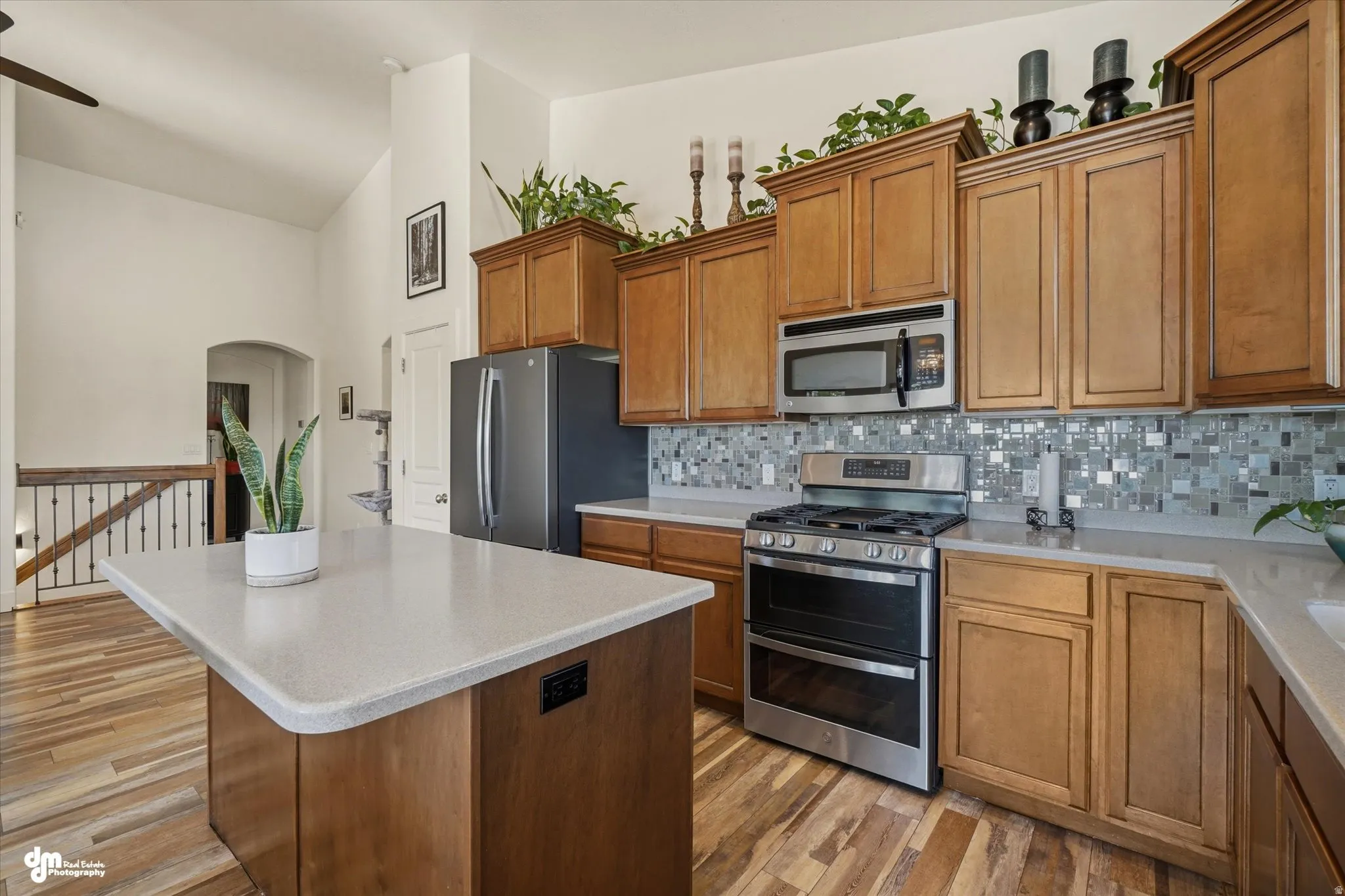Kitchen featuring wood-finish flooring, light wood cabinetry, stainless steel appliances, and a mosaic tile backsplash