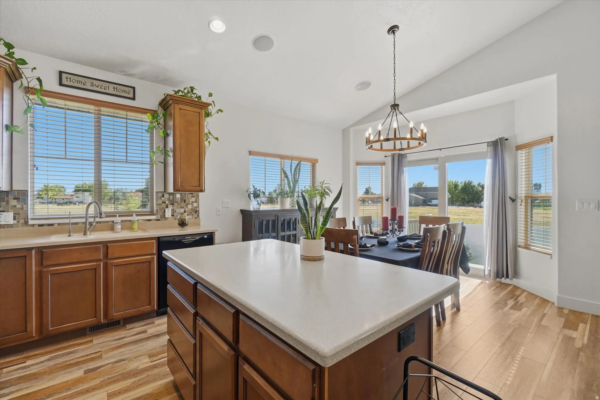 Kitchen and dining area featuring a central island with a light-toned countertop, wood-finish flooring, and vaulted ceilings