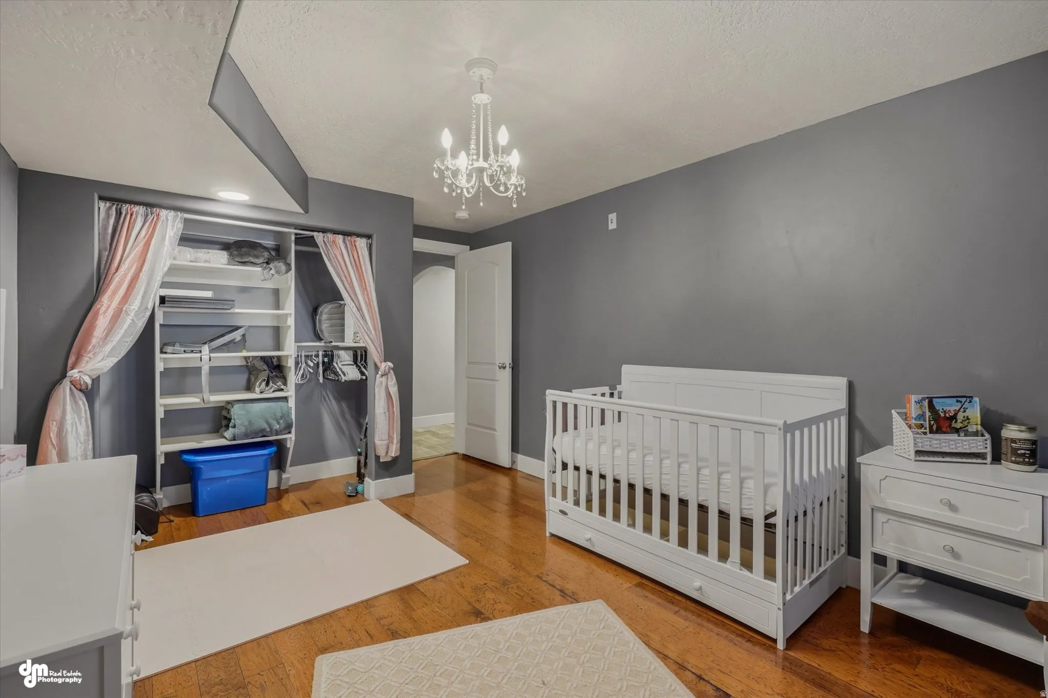 Hardwood flooring throughout featuring a built-in closet organization system, a white crystal chandelier, and a white paneled door