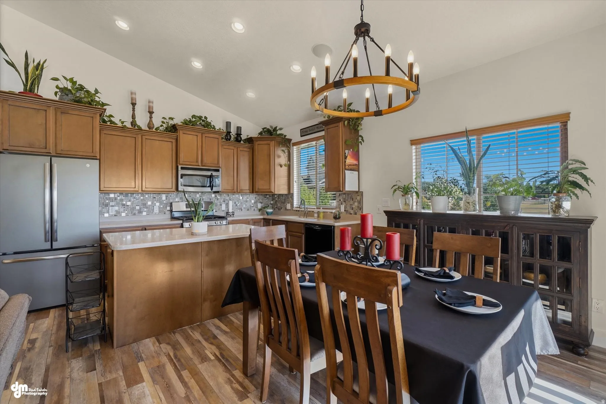 Open-concept kitchen and dining area featuring vaulted ceilings with recessed lighting, wood-finish flooring, light wood cabinetry, and a mosaic tile backsplash
