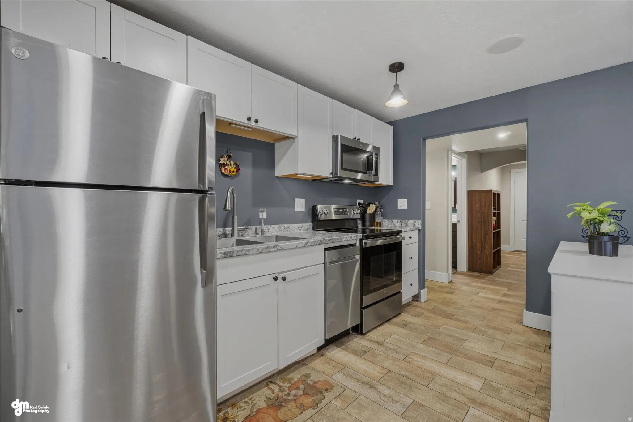 Kitchen featuring wood-finish flooring, white cabinetry with dark hardware, stainless steel appliances, granite-look countertops, and a single basin sink with a gooseneck faucet