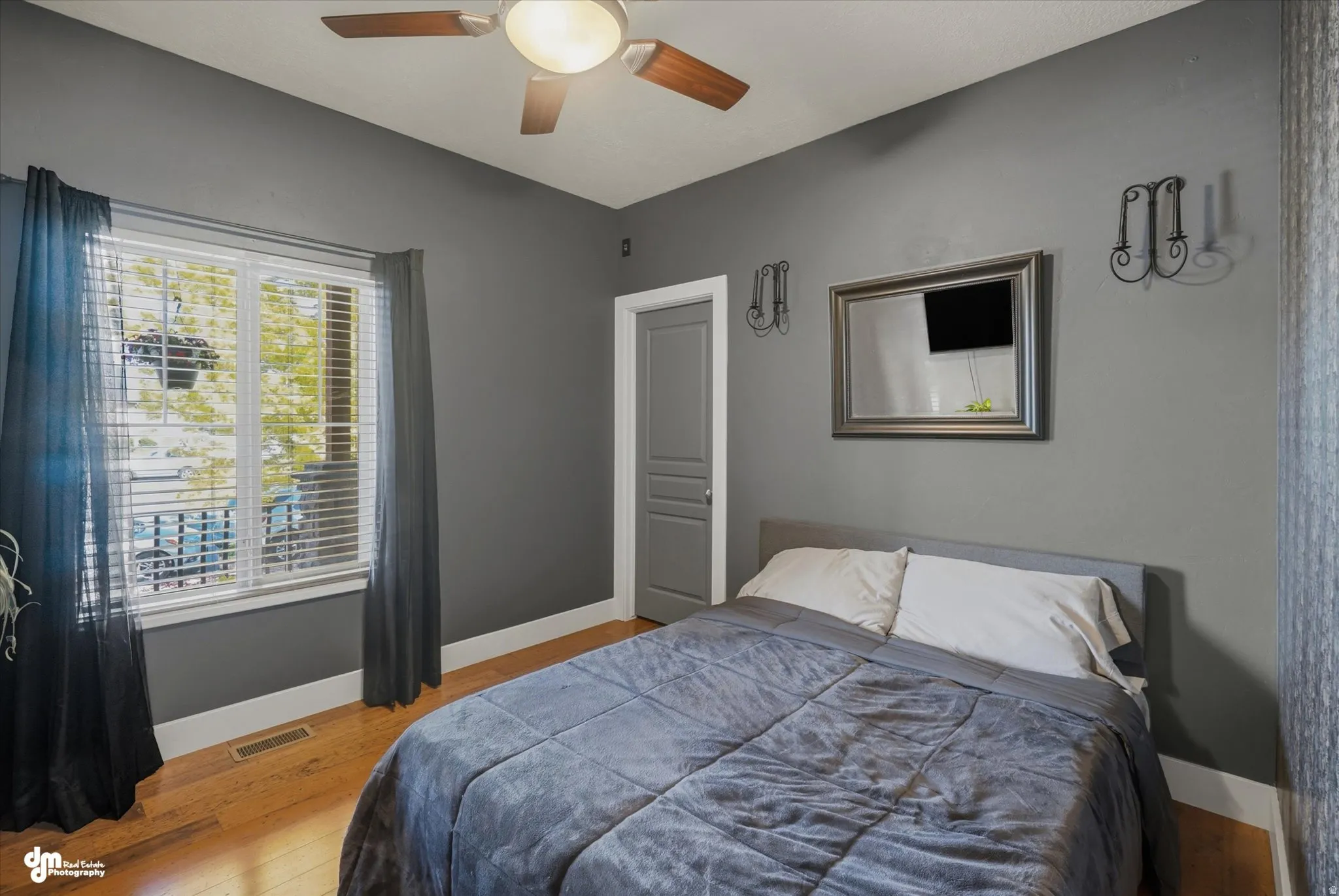 Spacious room featuring wood-finish flooring, a ceiling fan with integrated lighting, a large window with blinds, and a paneled door