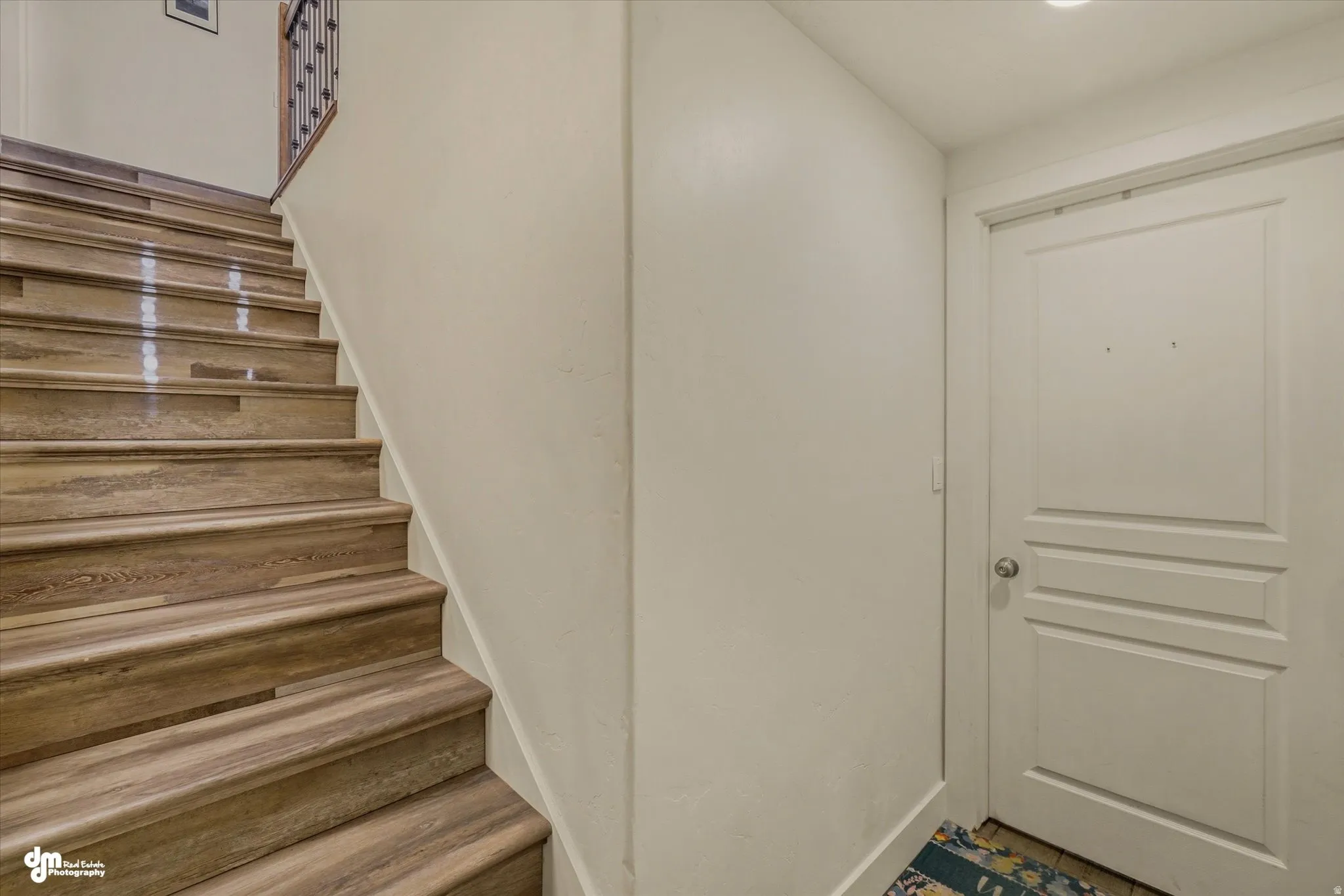 Staircase featuring wood-finish treads and risers, a wrought iron banister, and a wood handrail