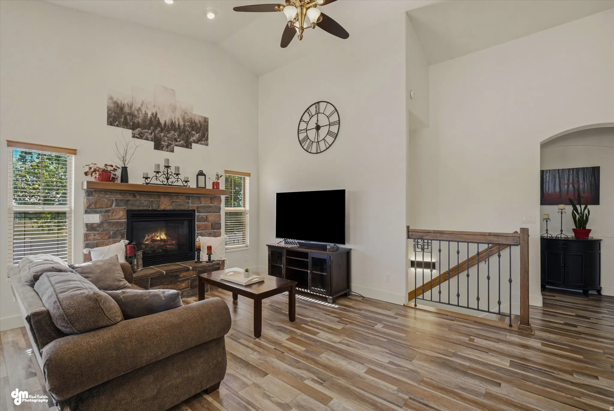Spacious living area featuring a stone-faced fireplace with wood mantel, vaulted ceilings, and wood-finish flooring