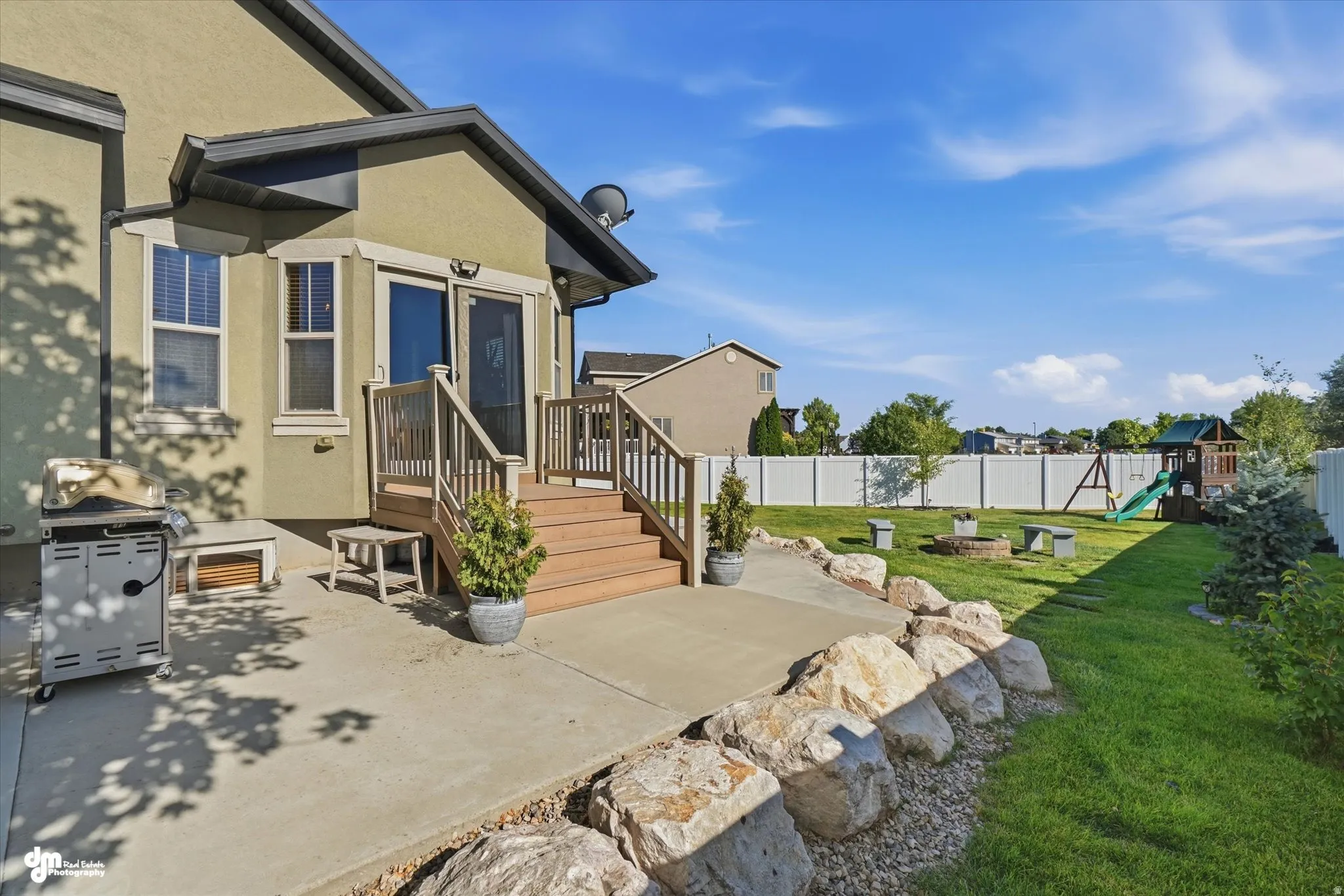 Expansive backyard featuring a manicured lawn, concrete patio, and rock landscaping
