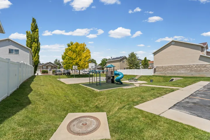 Expansive green space featuring a playground structure with a slide, a basketball court, and a picnic table