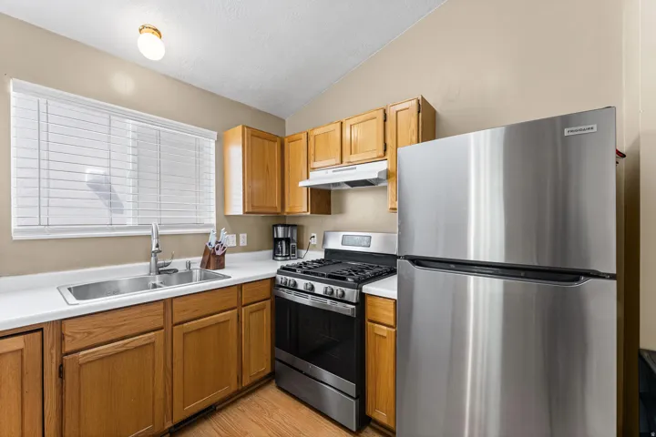 Kitchen featuring stainless steel appliances, wood-finish cabinetry, a double basin sink, and a window with horizontal blinds