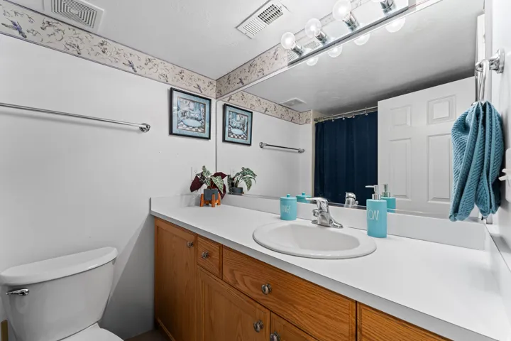 Bathroom featuring a wood-finish vanity with ample storage, a white countertop, an oval undermount sink, and a large wall-mounted mirror