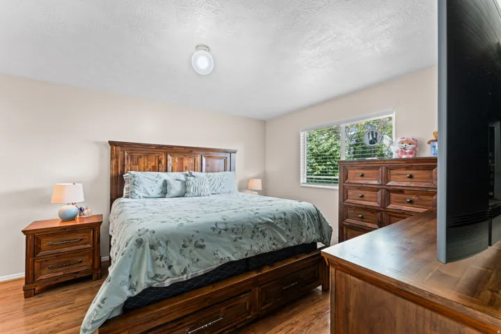 Wood-finish flooring anchors this room, featuring a window with blinds, light-toned wall paint, and a ceiling-mounted light fixture