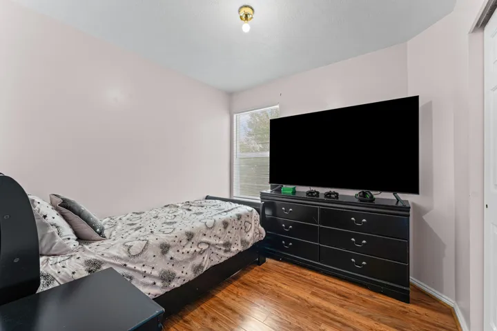 Bedroom featuring wood-finish flooring, a single window with horizontal blinds, and a built-in light fixture