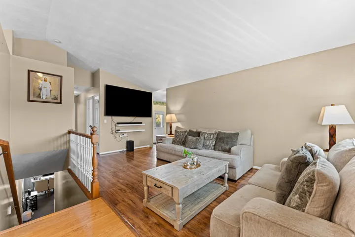 Open concept living area featuring vaulted ceilings, wood-finish flooring, and neutral wall tones