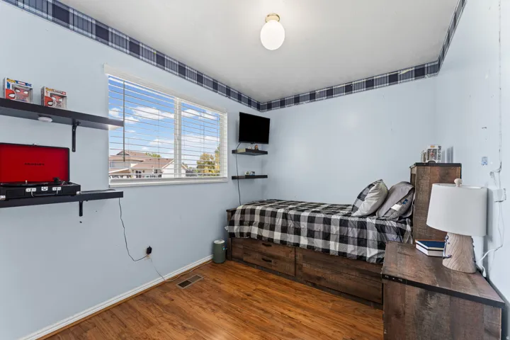 Bedroom featuring wood-finish flooring, a double window with blinds, and light blue wall color